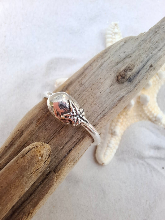 Silver ring featuring a delicate silver starfish hugging a silver pebble