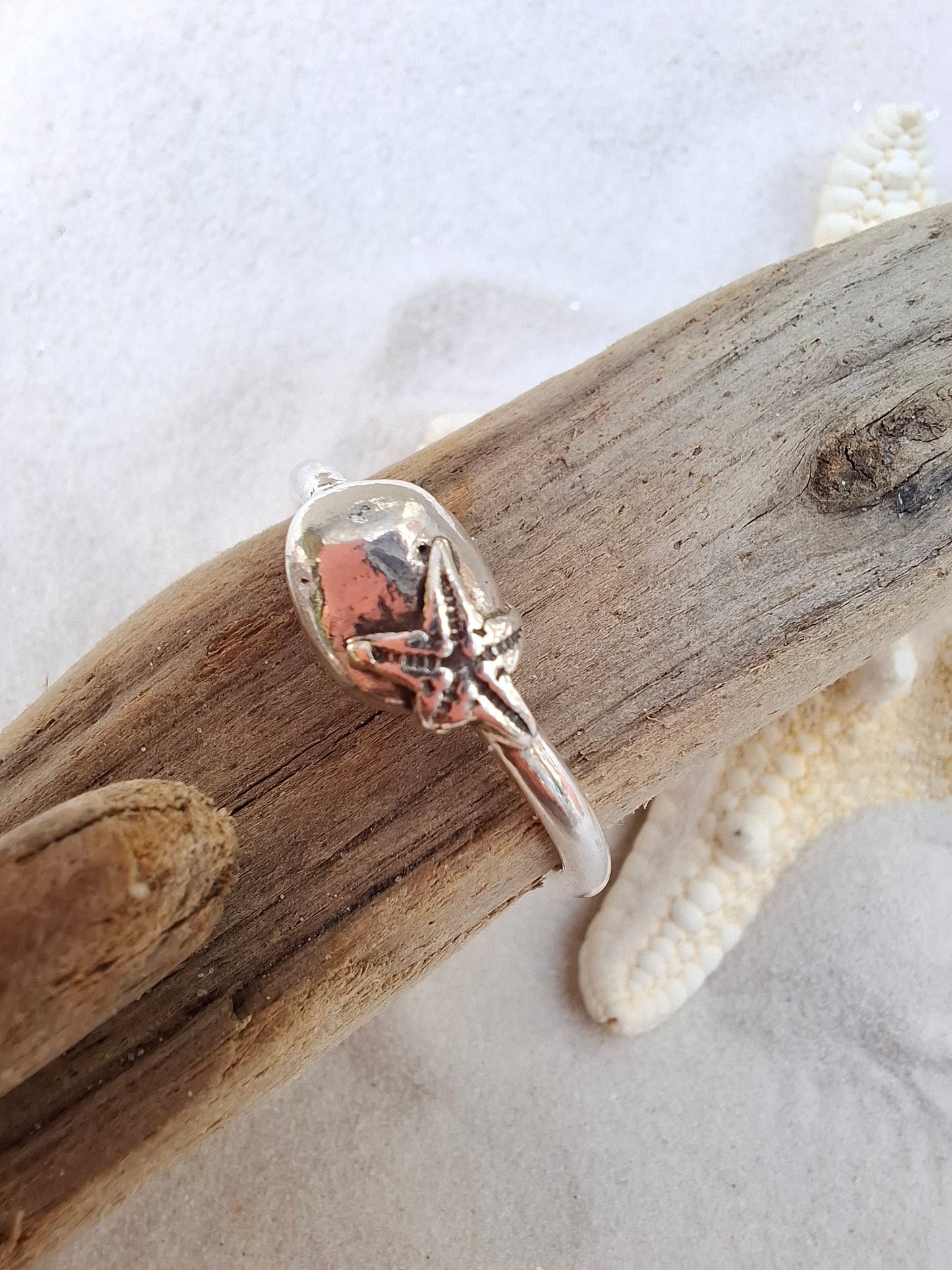 Silver ring featuring a delicate silver starfish hugging a silver pebble