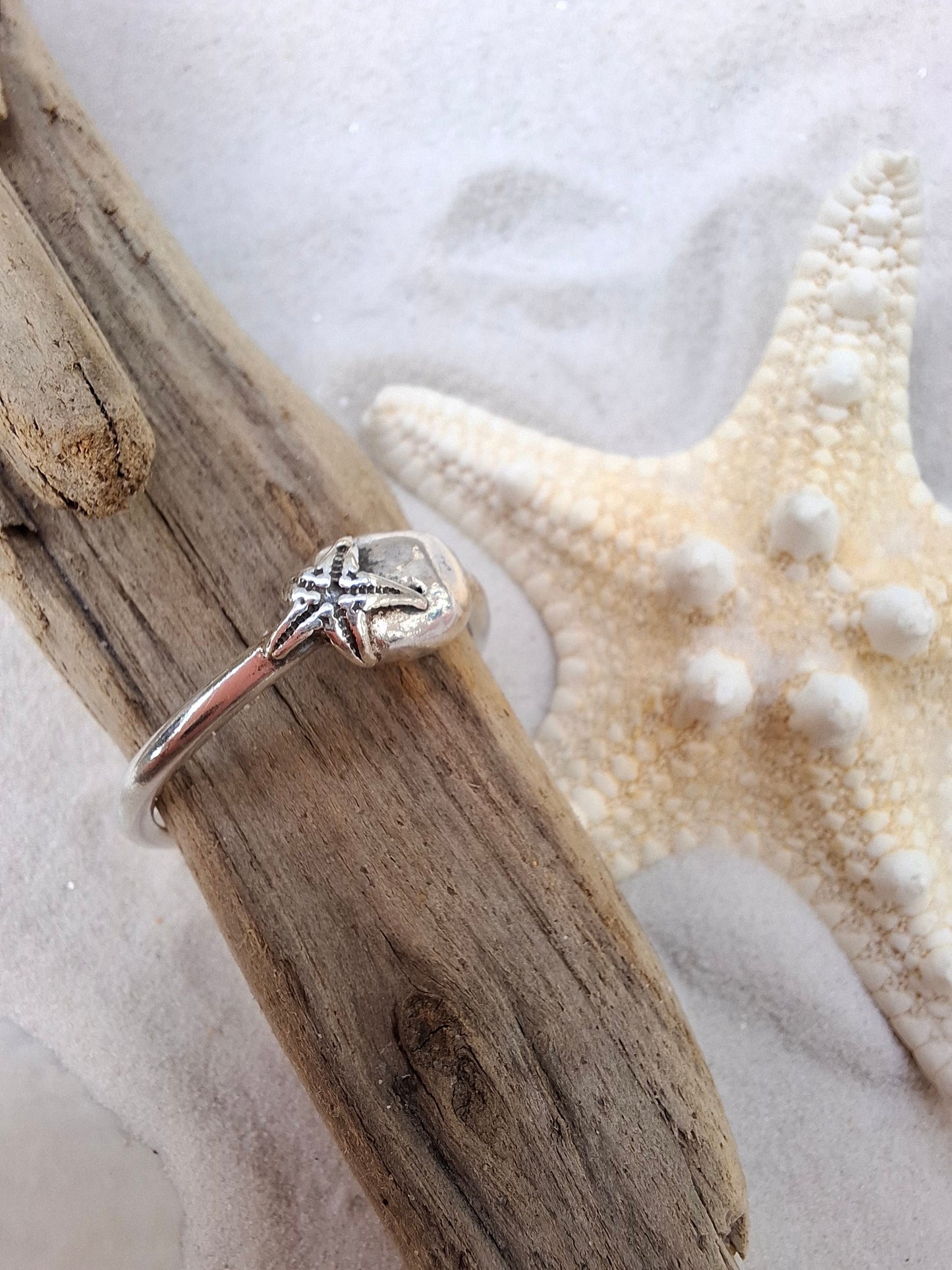 Silver ring featuring a delicate silver starfish hugging a silver pebble