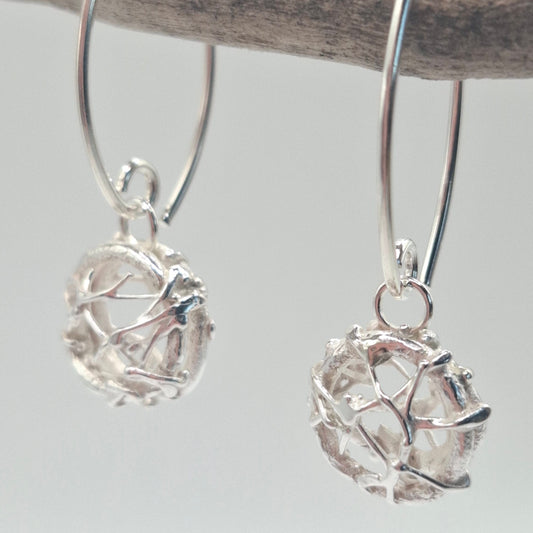 Dangly silver earrings by Shelley Ide Jewellery featuring intricate designs, hanging from ear hooks in a close-up shot.
