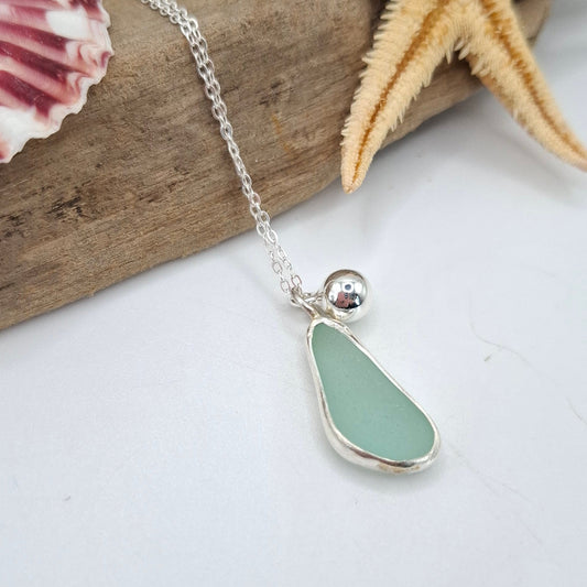 Necklace with a sea glass pendant on a piece of driftwood with a starfish and shell.