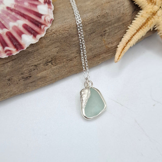 Necklace with a heart-shaped sea glass pendant on a piece of driftwood with a starfish and shell.