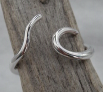 A pair of polished silver huggie hoop earrings with a twisted, fluid wave design, displayed on a piece of weathered wood against a neutral gray background.