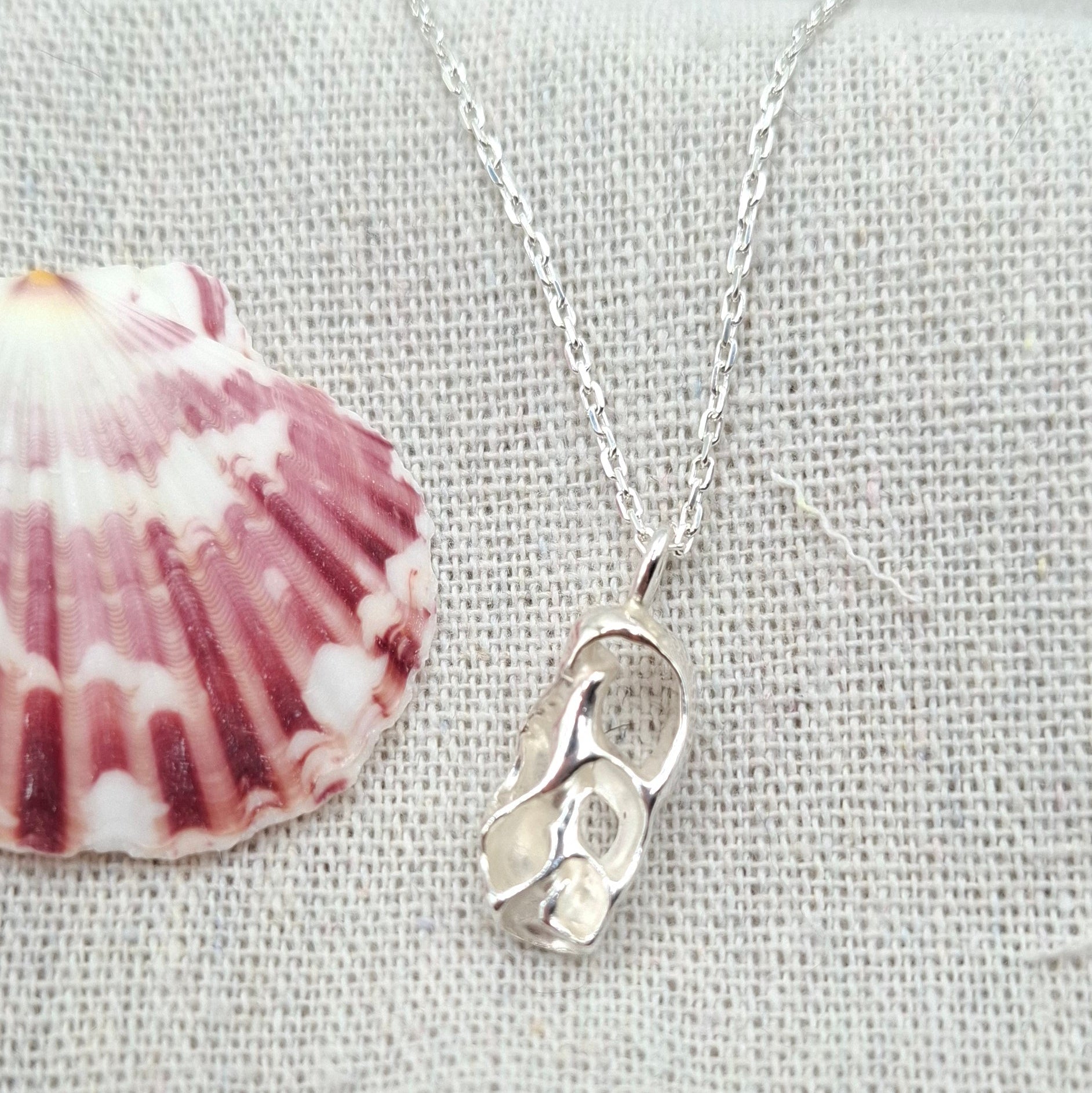 Silver necklace with a heart charm and shell pendant on a gray fabric background