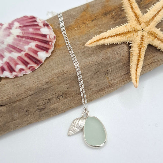 Necklace with a sea glass pendant on a piece of driftwood with a starfish and shell.