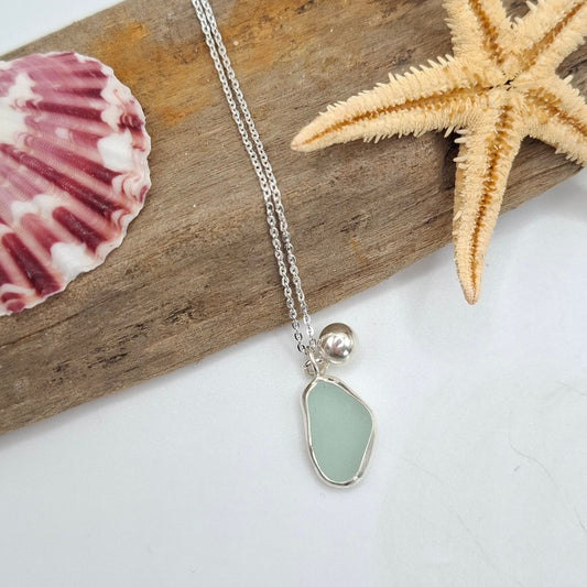 Necklace with a sea glass pendant on a piece of driftwood with a starfish and shell.