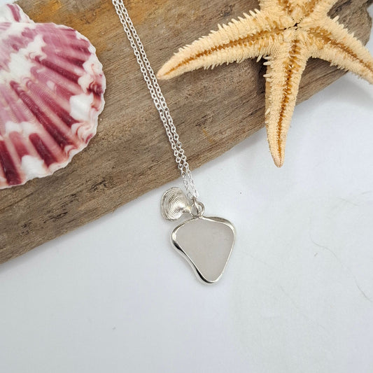 Silver necklace with a heart pendant on a piece of driftwood with a starfish and shell.