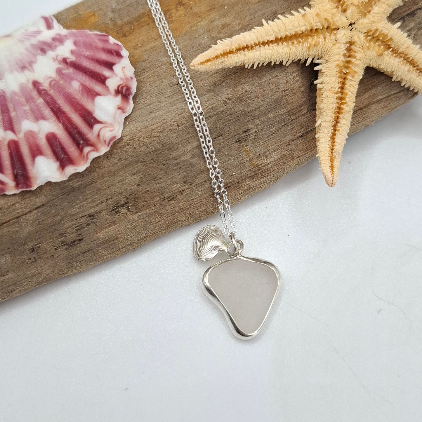 Channel Islands white seaglass pendant with silver clam charm on necklace by Shelley Ide Jewellery, close-up of pendant and charm.