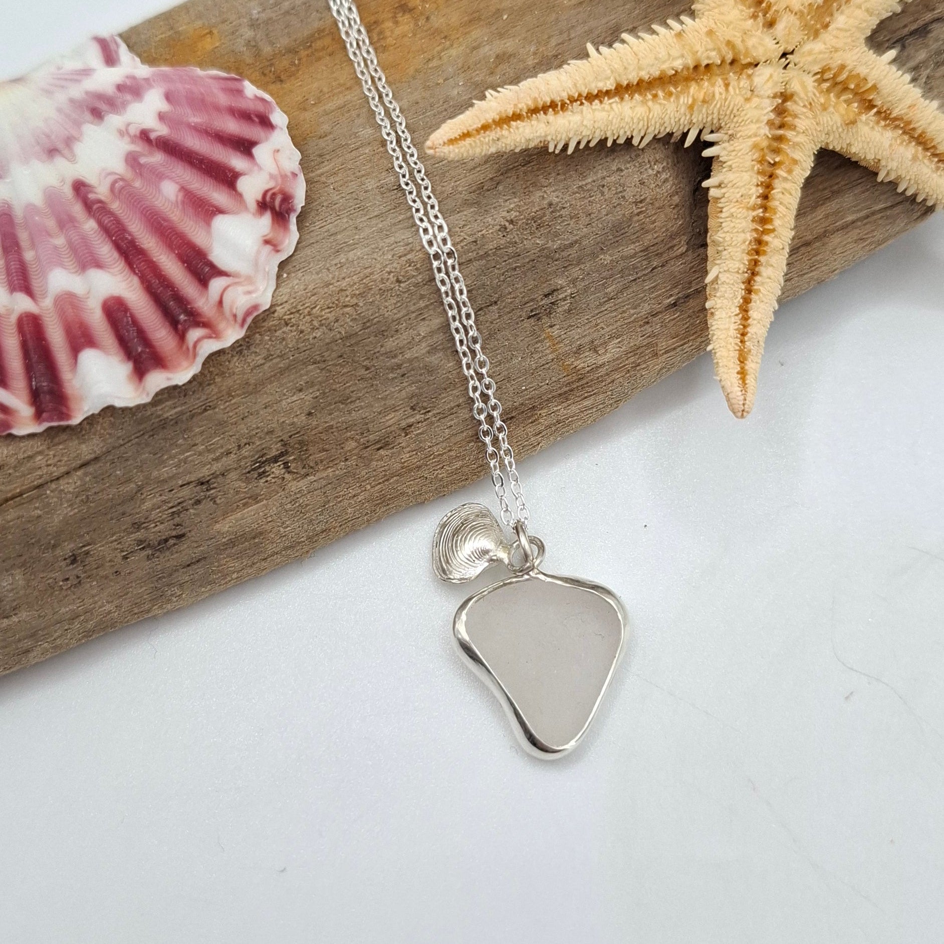 Channel Islands white seaglass pendant with silver clam charm on necklace by Shelley Ide Jewellery, close-up of pendant and charm.