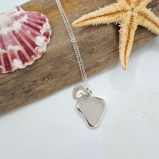 Silver heart-shaped pendant on a chain with a starfish and shell on a wooden stick against a white background