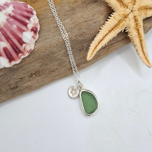 Necklace with a green teardrop pendant on a wooden board with a starfish and shell.