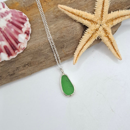 Necklace with a green pendant on a piece of driftwood with a starfish and shell.