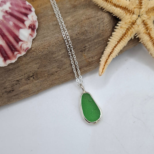 Necklace with a green pendant on a piece of driftwood with a starfish and shell.