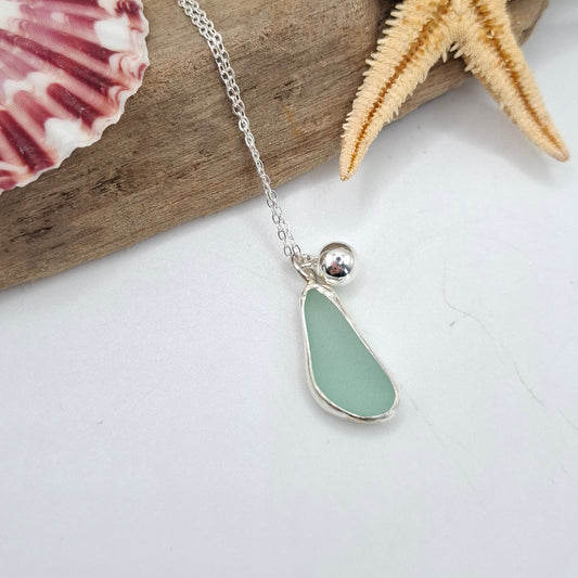 Necklace with a sea glass pendant on driftwood with a starfish and shell.