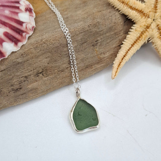 Necklace with a heart-shaped green pendant on a piece of driftwood with a starfish and shell.