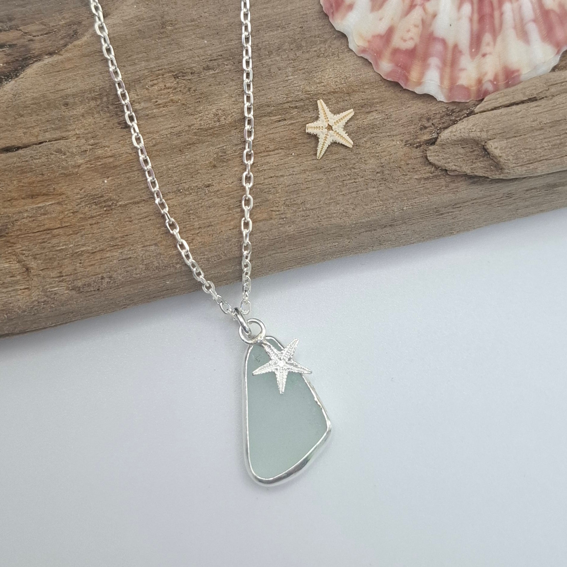 Silver bracelet with heart and star charms on a wooden stick with a shell