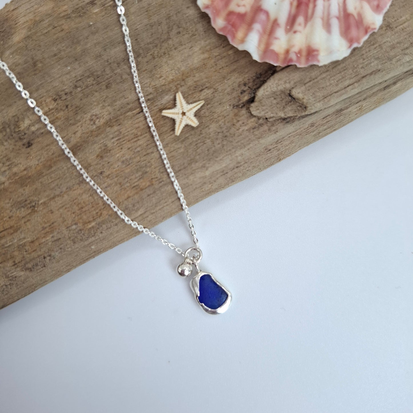 Necklace with a blue pendant on a wooden surface with a shell and starfish.