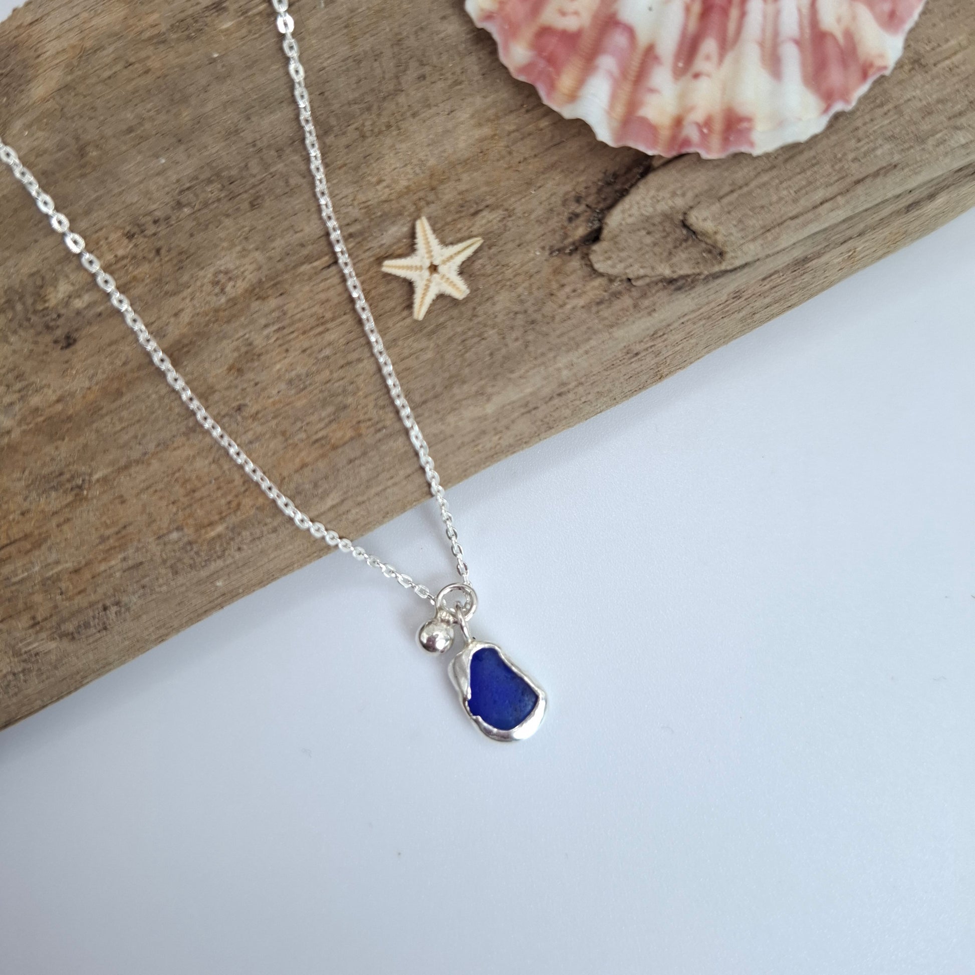 Necklace with a blue pendant on a wooden surface with a shell and starfish.
