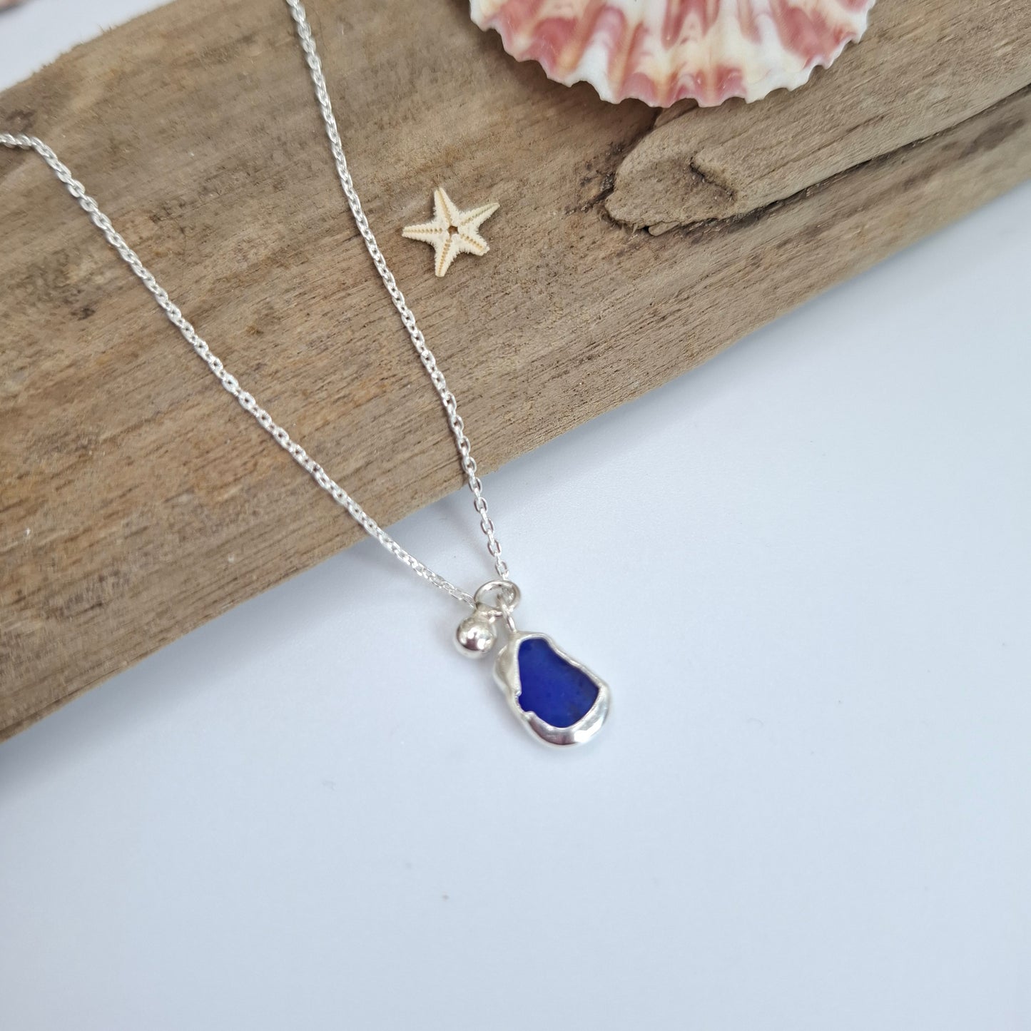 Silver necklace with a blue heart pendant on a wooden surface with a shell and starfish.